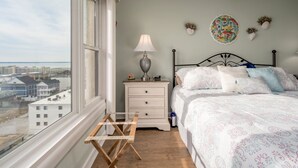A bedroom with a bed, a nightstand, a lamp, and a view of buildings through a window.