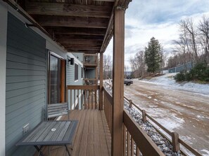 A wooden deck with a table and chairs, a covered porch, and a view of a snowy road. - White Cap B-318 - Sunday River Condo (Newry)