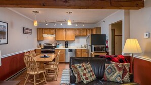 A compact living space with a dining area, kitchen, and a leather sofa with patterned cushions.