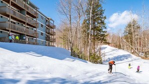 A ski resort with a multi-story building, a snow-covered slope, and a forested area.