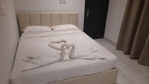 A neatly made bed with a heart-shaped towel arrangement, a dark door, and beige curtains. - Atlantis Hotel Suites (Salmiya)