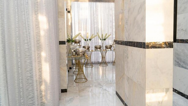 A luxurious hallway with marble flooring, a glass table with gold wire chairs, and a large window with sheer curtains. - Atlantis Hotel Suites (Salmiya)