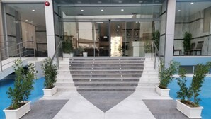 A modern building entrance with a glass facade, a set of stairs leading to a door, and potted plants on either side. - Atlantis Hotel Suites (Salmiya)