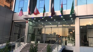 A modern building with multiple flags, including the American flag, and a glass entrance with steps leading up to it. - Atlantis Hotel Suites (Salmiya)