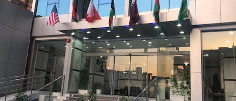 A modern building with multiple flags, including the American flag, and a glass entrance with steps leading up to it.