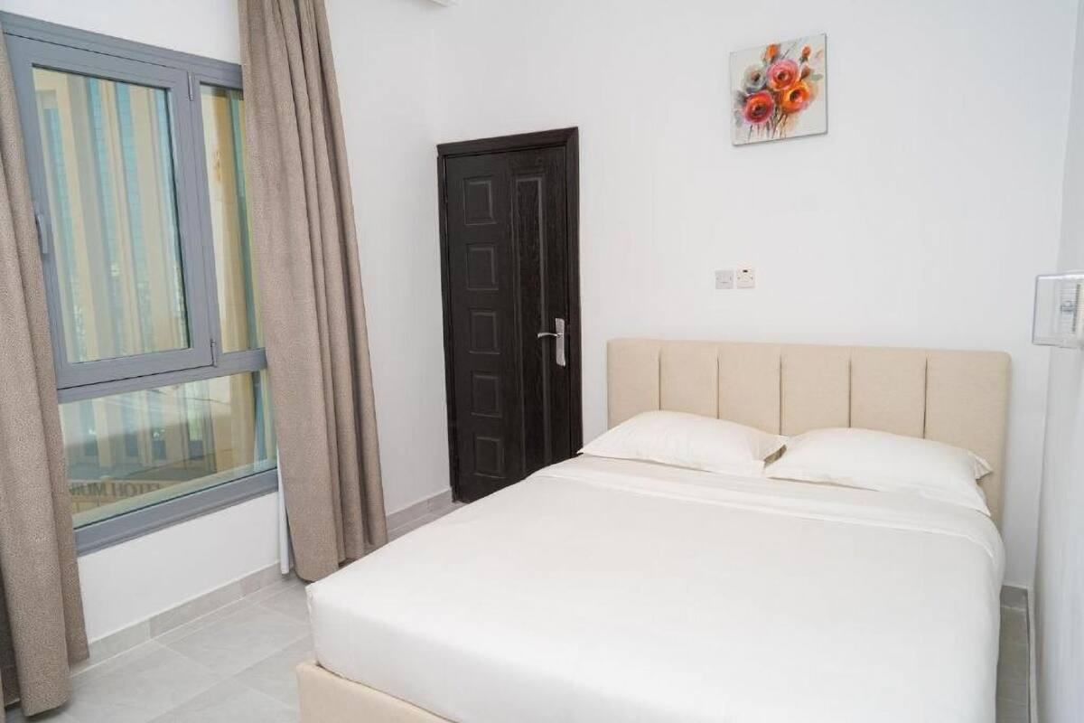 A bedroom with a bed, a window with curtains, a door, and a painting on the wall.