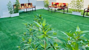 A rooftop terrace with green artificial grass, two seating areas with patterned cushions, and potted plants. - Atlantis Hotel Suites (Salmiya)