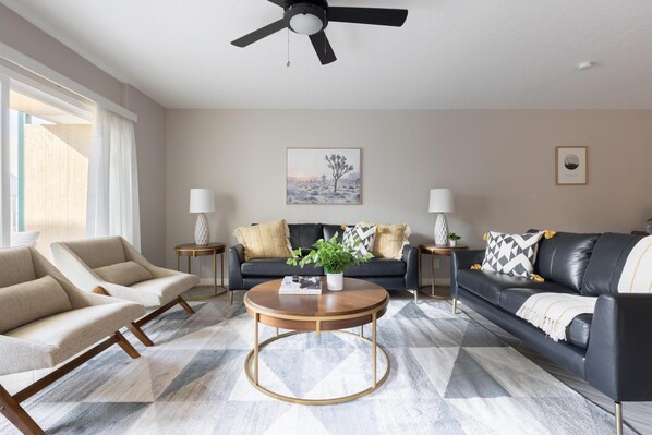 A living room with a black leather sofa, beige armchairs, a round coffee table, and a ceiling fan. - Modern Chic Condo In Midtown w/ Pool & Hot Tub (Phoenix)