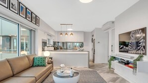 Una sala moderna con un sofá, una mesa de centro y un televisor sobre un mueble blanco.