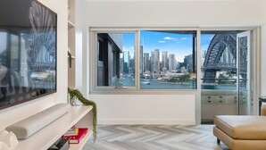 Una sala de estar moderna con un amplio ventanal que ofrece vista a la ciudad, incluyendo un puente y rascacielos.