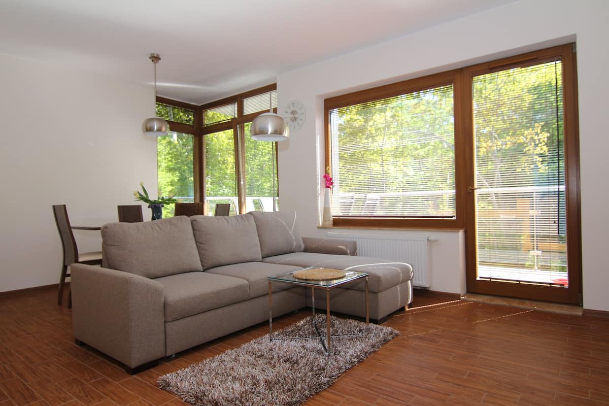 A modern living room with a sectional sofa, a glass coffee table, and large windows with blinds.
