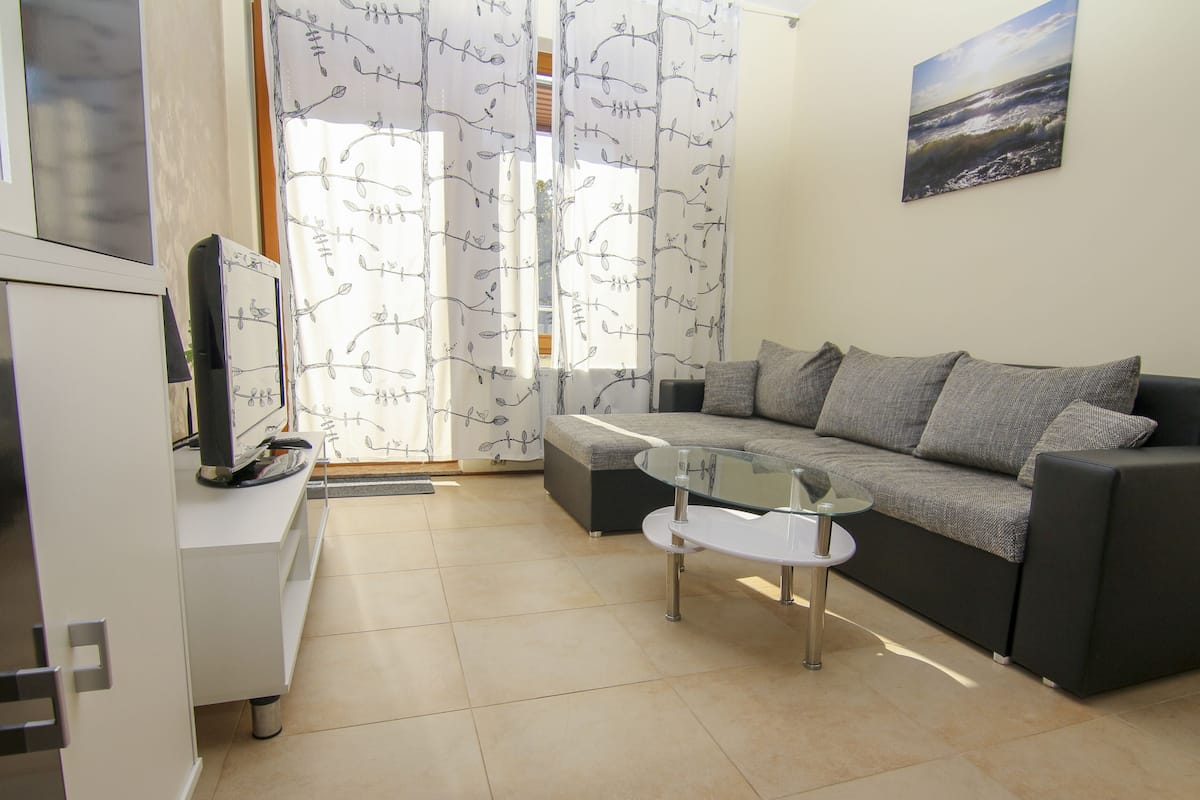 A modern living room with a grey sofa, a glass coffee table, and a flat-screen TV on a white cabinet.