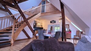 Un loft amplio con escalera de madera, comedor y una zona de estar acogedora con sofá y cojines.