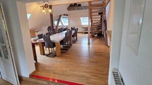 Un comedor con una larga mesa de madera y sillas, una escalera de madera y vistas al exterior a través de tragaluces.