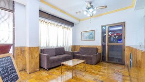 A reception area with a wooden floor, two sofas, a coffee table, a ceiling fan, a window with curtains, and a signboard. - Hotel Astoria Real (Cali)