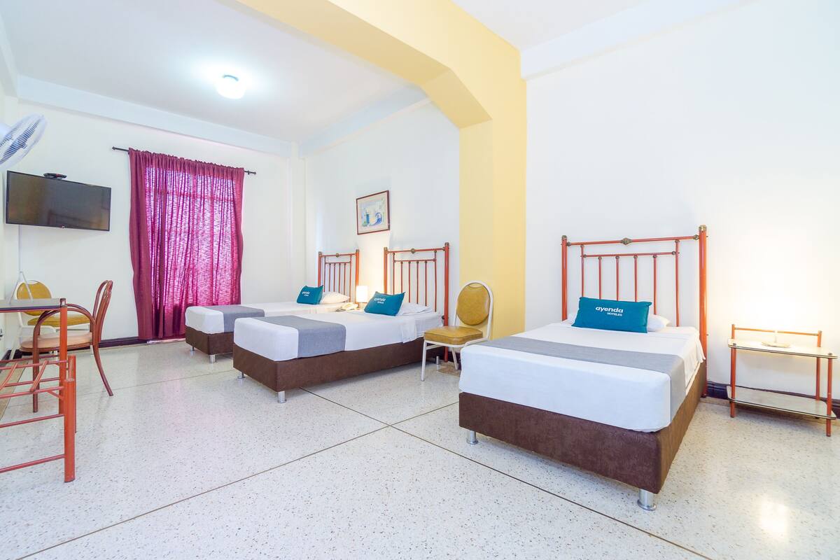 Quarto de hotel com duas camas, televisão, cadeira e escrivaninha.