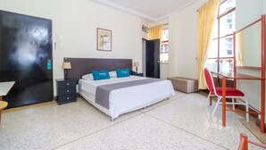 A hotel room with a bed, a desk, a chair, a wardrobe, and a window with curtains. - Hotel Astoria Real (Cali)