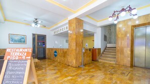 A reception area with a sign for a restaurant terrace, a reception desk, a staircase, and a ceiling fan. - Hotel Astoria Real (Cali)