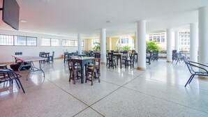 A spacious indoor area with multiple tables and chairs, large windows, and a flat-screen TV mounted on the wall. - Hotel Astoria Real (Cali)