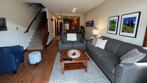 Ein Wohnzimmer mit einer Couch, einem blauen Sessel, einem Couchtisch und einer Treppe, die in eine Küche führt.