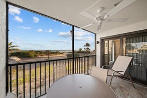 A balcony with a table and chairs, a ceiling fan, and a view of the beach and ocean. - Pelicans Roost 107: Corner Unit with Gulf Views! (Sanibel)