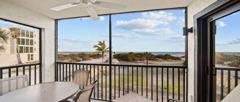 A balcony with a table and chairs, a ceiling fan, and a view of the beach and ocean.