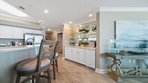 A modern kitchen with white cabinets, a central island with bar stools, and a glass display shelf.