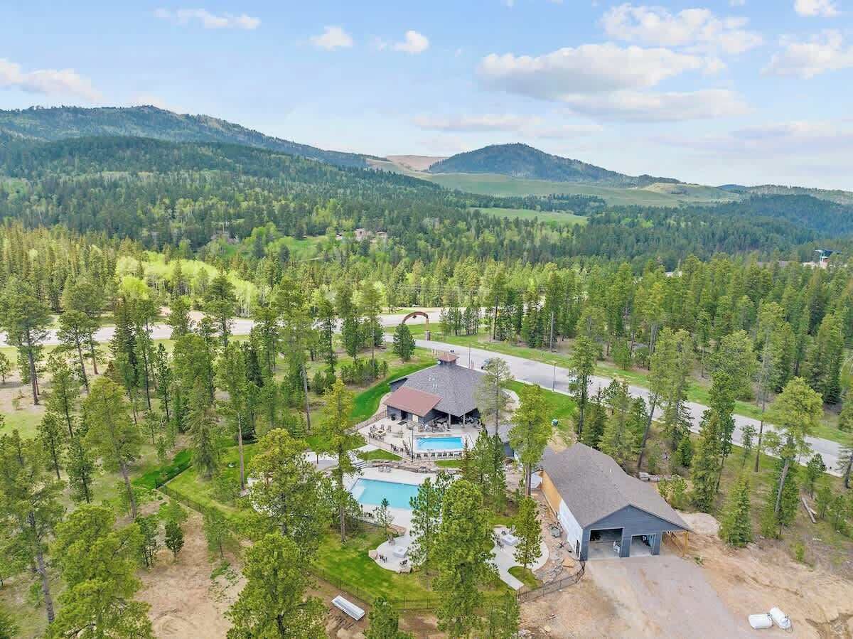 Ein Luftbild zeigt einen Urlaubsort mit Schwimmbad, überdachter Terrasse und einem großen Gebäude, das von dichtem Wald und Hügeln umgeben ist.