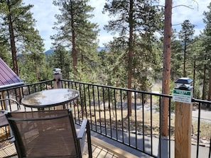 Enjoy a peaceful retreat on this deck surrounded by tall pine trees, featuring a small table and chair.
