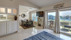 A spacious living room with a dining area, a TV, and a balcony with a view of the water. - Dock Holiday 2 Bedroom Condo by Redawning (Rockport)
