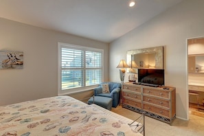 A bedroom with a bed, a dresser, a chair, a TV, and a window with blinds. - Dock Holiday 2 Bedroom Condo by Redawning (Rockport)