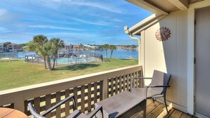 A balcony with wicker chairs, a pool, and a view of a lake and buildings. - Dock Holiday 2 Bedroom Condo by Redawning (Rockport)