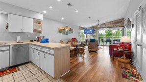 A modern kitchen with white cabinets, a dining area with wooden chairs, and a red sofa. - Fairway Heights 2 Bedroom Condo by RedAwning (Branson)