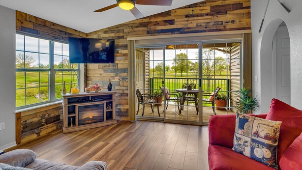A spacious living room with a fireplace, a ceiling fan, and a large sliding glass door leading to an outdoor patio. - Fairway Heights 2 Bedroom Condo by RedAwning (Branson)