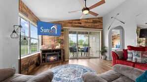 A spacious living room with a fireplace, a ceiling fan, and a large window. - Fairway Heights 2 Bedroom Condo by RedAwning (Branson)