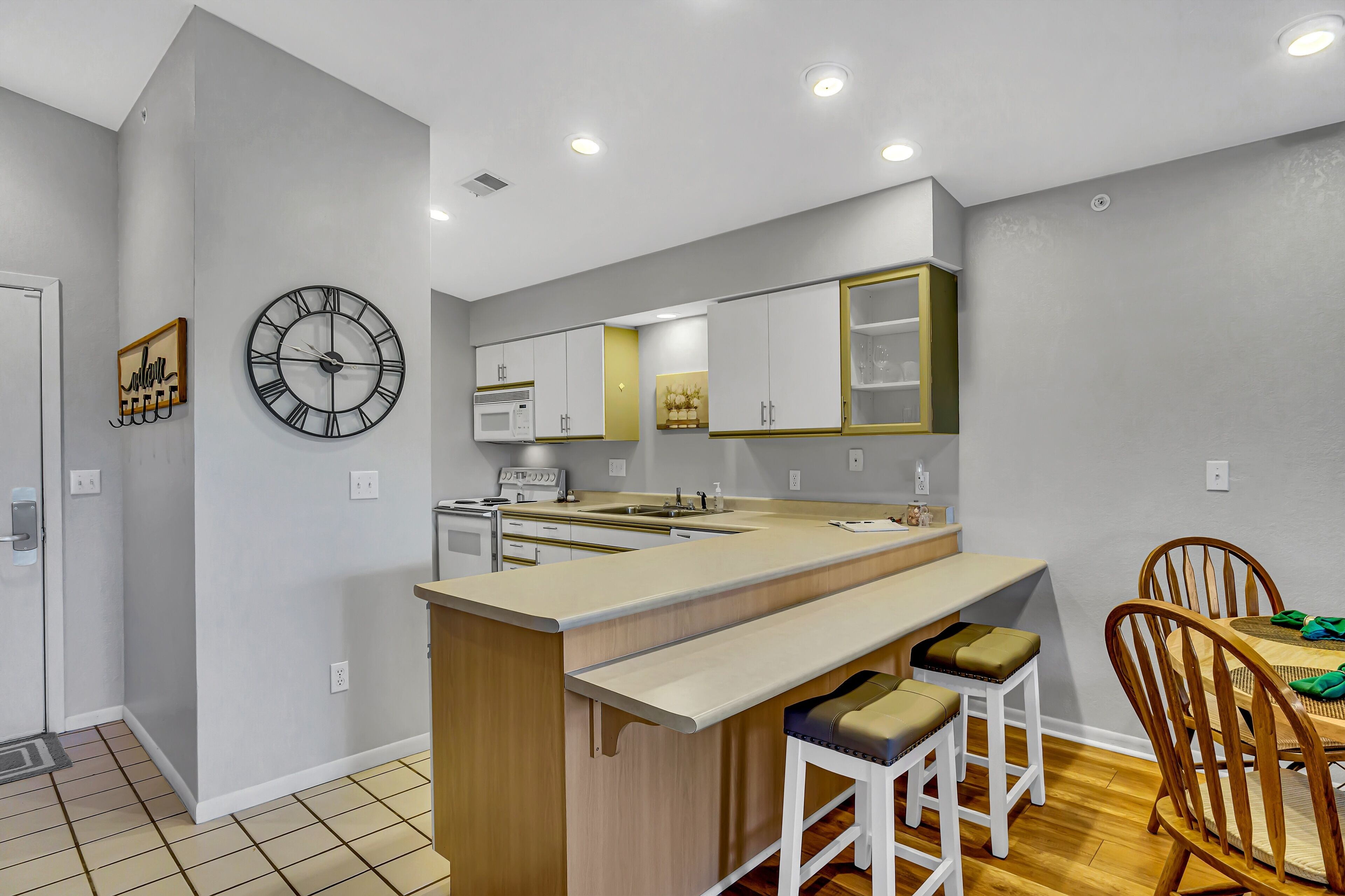 A modern kitchen with a central island, white cabinetry, and a large wall clock.