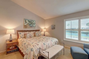Une chambre à coucher avec un lit, des lampes de chevet, un banc, une chaise et une fenêtre avec des stores.