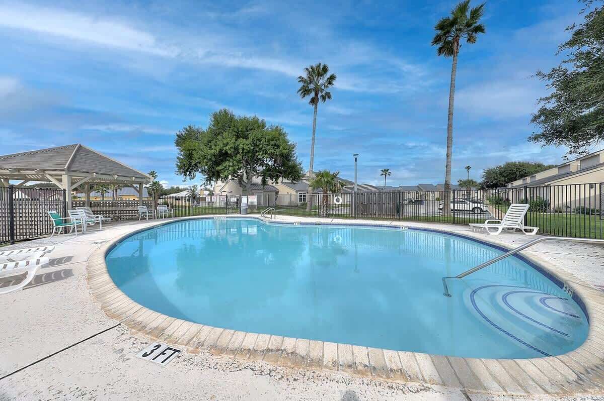 Une piscine avec des chaises longues, des palmiers et un espace abrité.