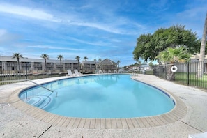 Une piscine avec des chaises longues, un espace délimité par une clôture et un bâtiment en arrière-plan.