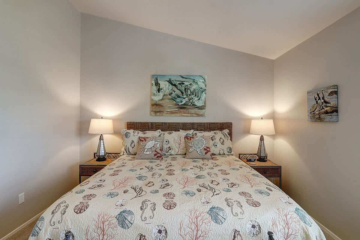 A bedroom with a bed, two bedside tables with lamps, a headboard, and two wall-mounted paintings.