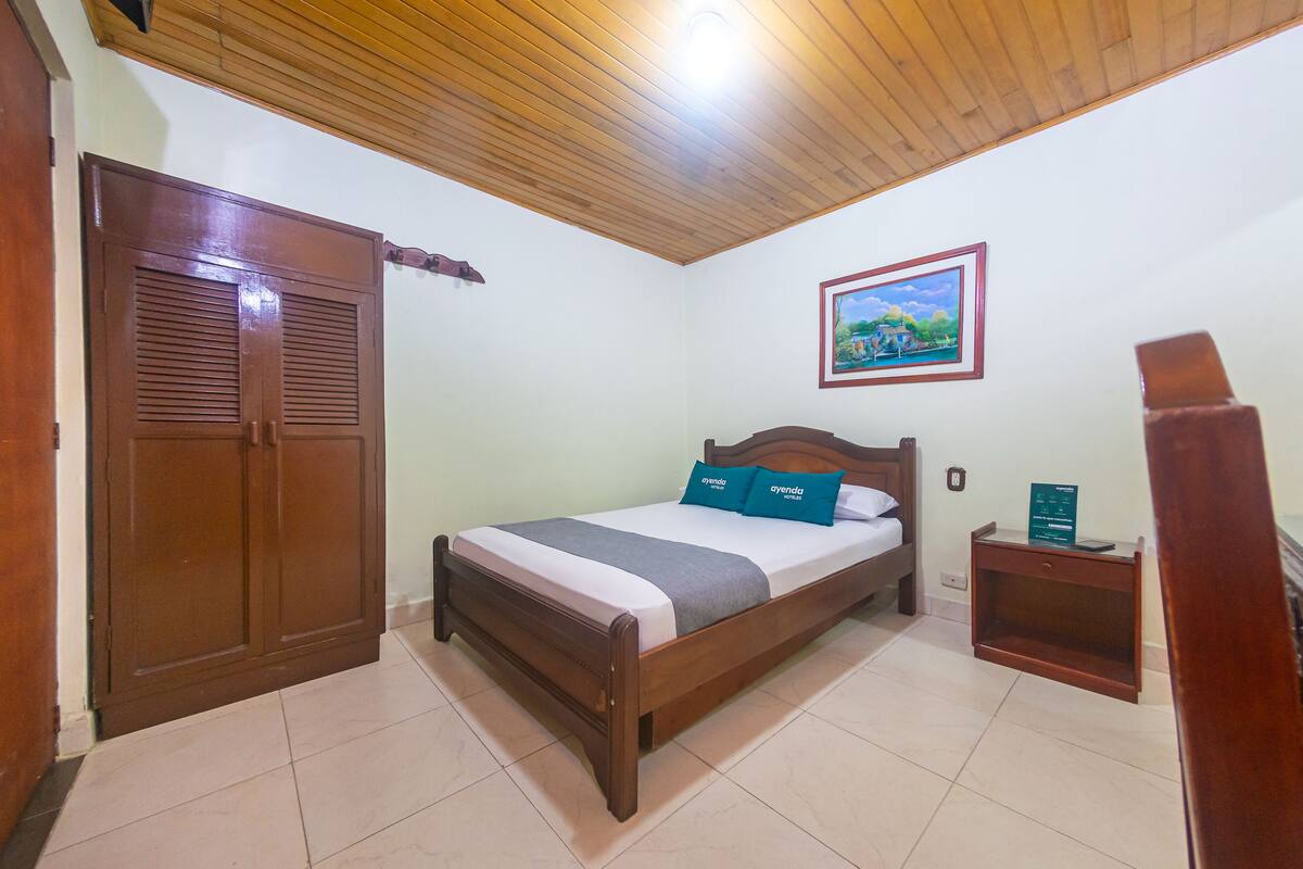A bedroom with a wooden bed, a nightstand, a wardrobe, and a painting on the wall.