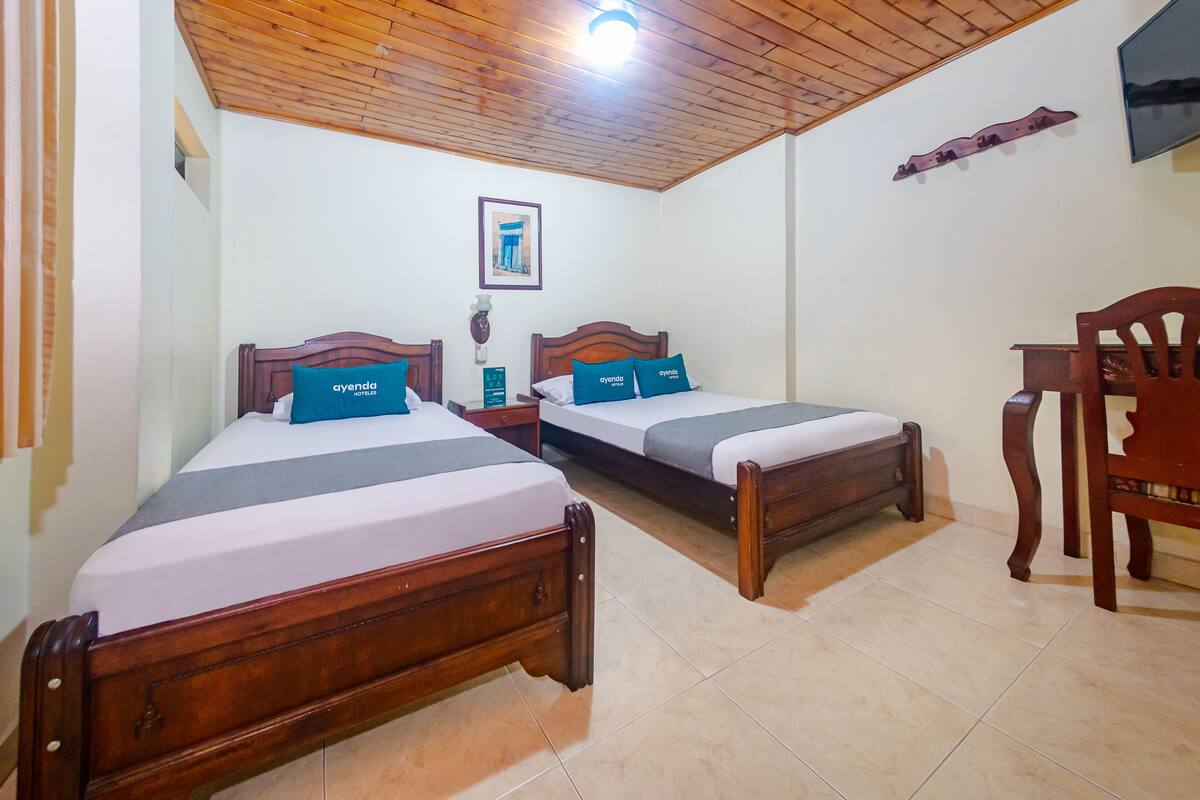 A hotel room with two wooden beds, a wooden chair, a flat-screen TV, and a framed picture on the wall.