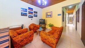 A hotel lobby with patterned orange sofas, a wooden ceiling, a television, and a hallway leading to other rooms. - Ayenda Pakande (Popayán)