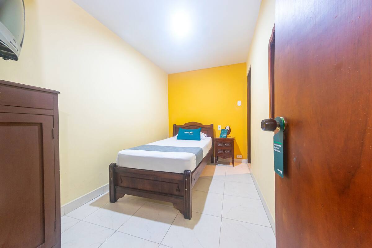 A bedroom with a bed, a nightstand, a wooden wardrobe, and a door with a sign.