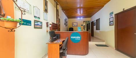 A reception desk with a sign reading "ayenda hotels" in a hotel lobby with tiled floors and wooden ceiling.
