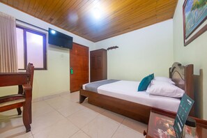 Habitación de hotel con techo de madera, cama con colchón blanco y almohada turquesa, silla de madera, armario de madera y televisor montado en la pared.