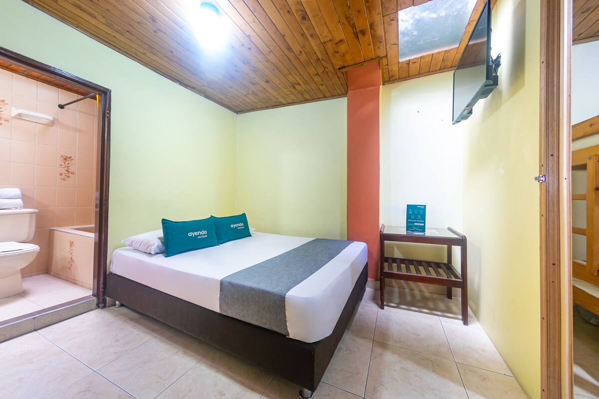 A bedroom with a bed, a wooden bench, a toilet, and a shower area.
