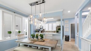 A dining area with a wooden table and benches, potted plants, and hanging light fixtures. - Tranquil Bay Views – Cedars East #812 by RVA (Longboat Key)