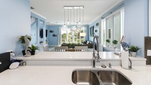 A modern kitchen with a central island, stainless steel sink, and pendant lighting. - Tranquil Bay Views – Cedars East #812 by RVA (Longboat Key)