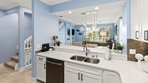 A modern kitchen with white cabinets, a stainless steel sink, and a large island. - Tranquil Bay Views – Cedars East #812 by RVA (Longboat Key)